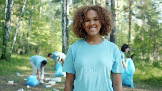 Young woman smiles while volunteers clean forest